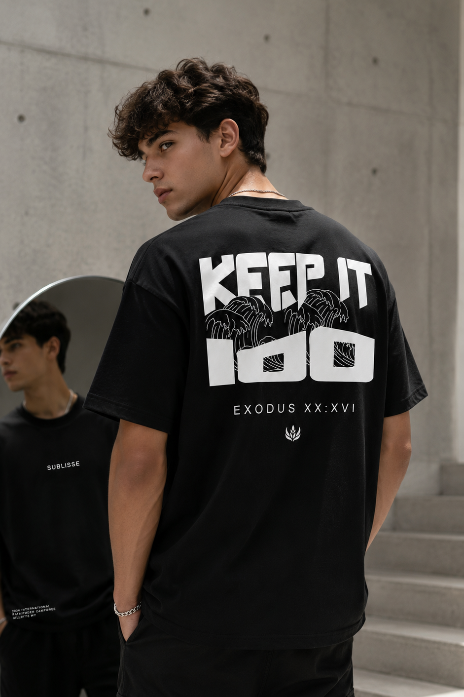Person wearing a black t-shirt with text on the back, standing in an urban setting.